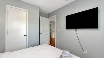 Un dormitorio con una cama, un televisor montado en la pared y una puerta que da a otra habitación.