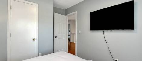 A bedroom with a bed, a TV mounted on the wall, and a door leading to another room.