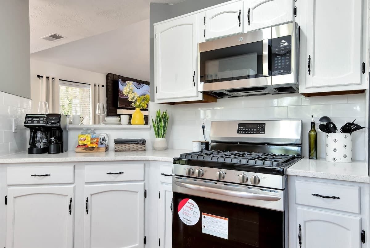 Una cocina moderna con armarios blancos, microondas, estufa y cafetera.