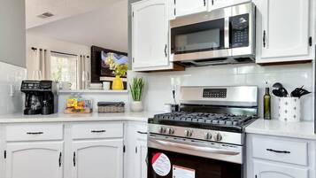 Una cocina moderna con armarios blancos, microondas, estufa y cafetera.