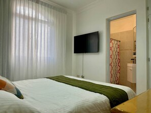 Ein Hotelzimmer mit einem Bett, einem an der Wand befestigten Fernseher und einem sichtbaren Duschbereich durch eine geöffnete Tür.