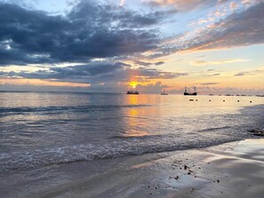 A beach with boats, a sunset, and a cloudy sky. - Walk to Beach · 1BR w/ Rooftop Jacuzzi (Punta Cana)