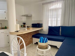 Um espaço compacto com cozinha compacta, sofá-cama, pequena mesa de jantar e uma cadeira.