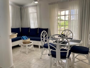 Quarto com sofá, mesa de jantar com cadeiras, mesa redonda pequena e janela com cortinas.