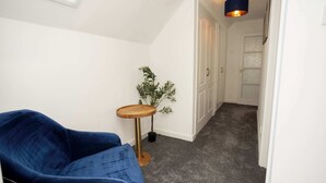 Ein Flur mit einem blauen Sofa, einem kleinen Holztisch mit einer Pflanze und einer Tür am Ende.