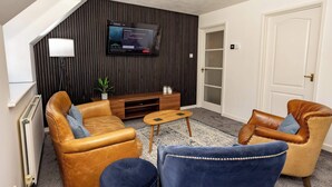 Ein modernes Wohnzimmer mit Ledersofas, einem Holztisch und einem Flachbildfernseher, der an einer dunklen Wand befestigt ist.