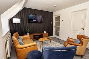 Ein modernes Wohnzimmer mit Ledersofas, einem Holztisch und einem Flachbildfernseher, der an einer dunklen Wand befestigt ist.