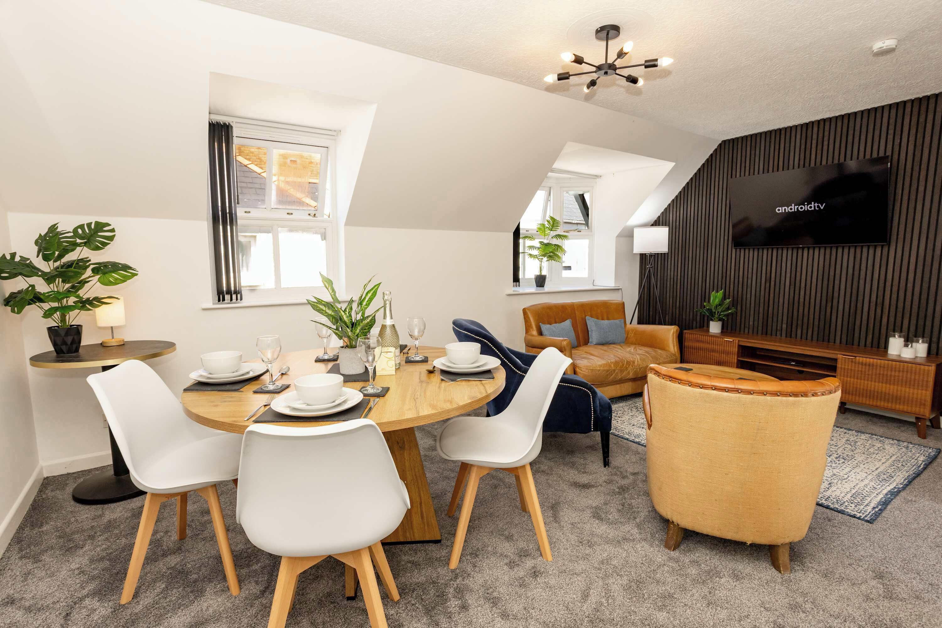 A modern living room with a dining area, a sofa, a TV, and a ceiling fan.