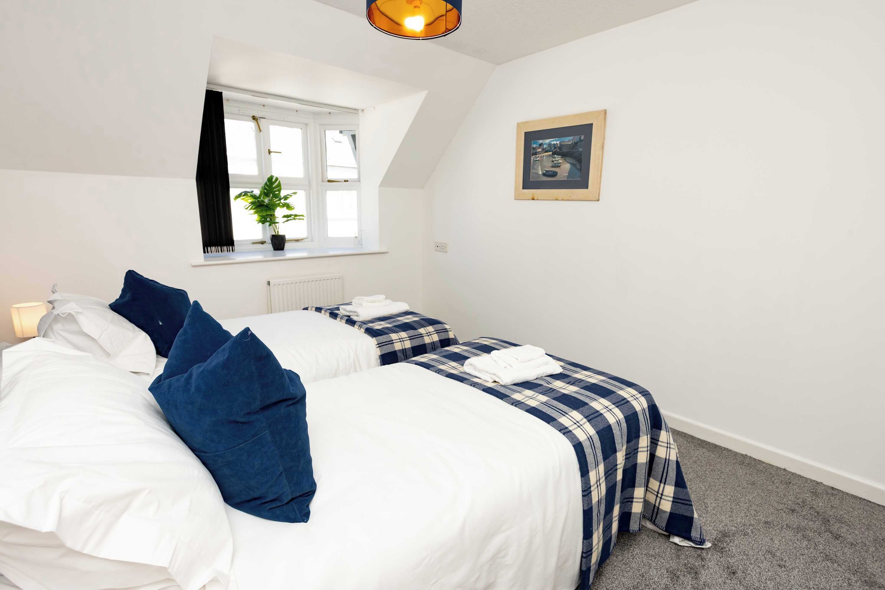 A bedroom with two beds, a window with curtains, a radiator, and a framed picture on the wall.