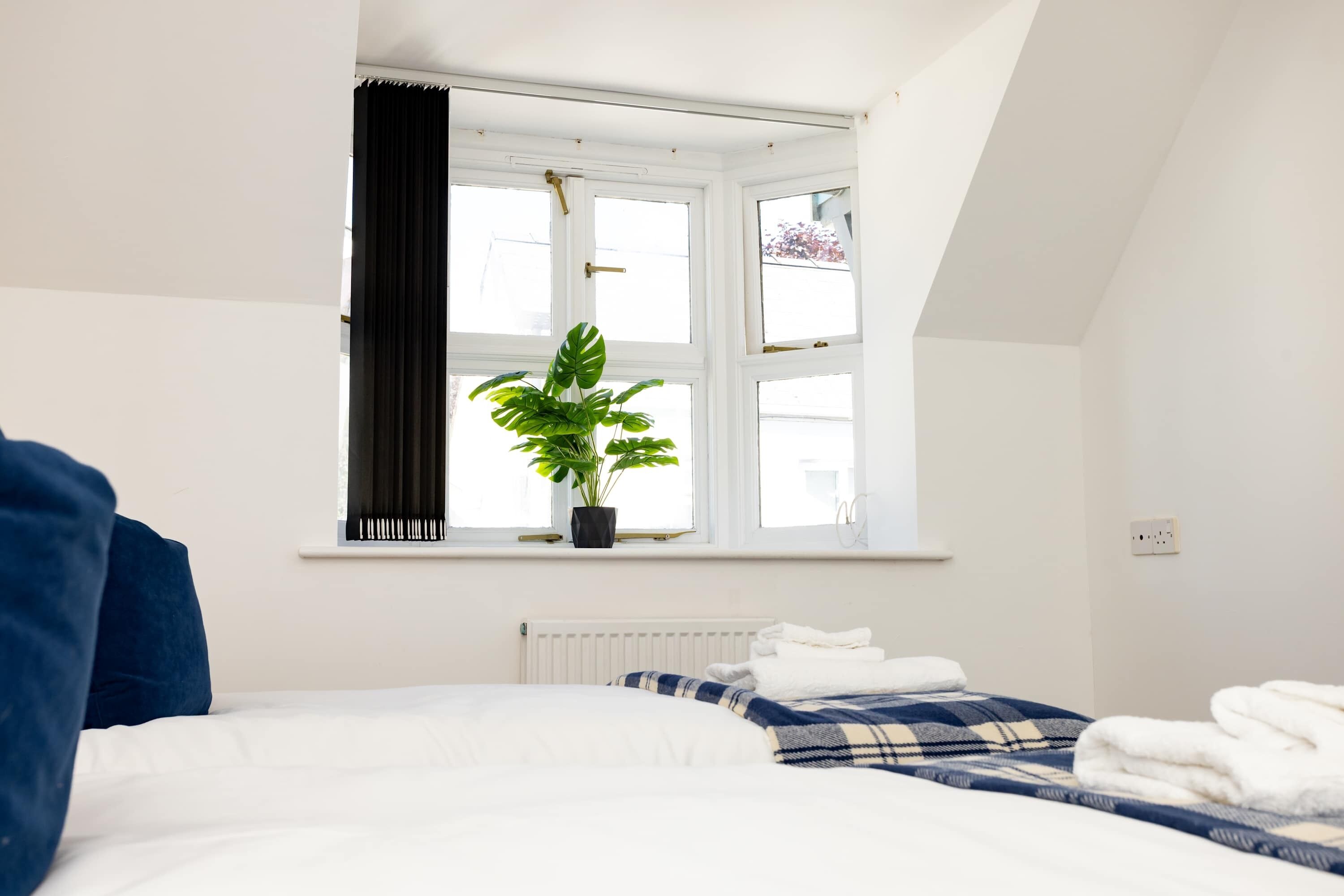 A bedroom with a bed, a window with curtains, a radiator, and a potted plant.