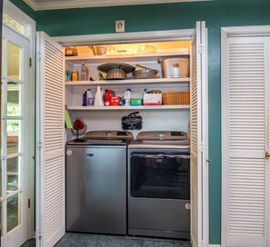 A compact kitchen with a refrigerator, stove, and shelves containing various kitchen items. - Charming waterfront getaway with great water access. (Tool)