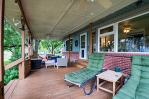A covered porch with wooden flooring, a green cushioned lounge chair, a small table, and a wicker sofa with red cushions. - Charming waterfront getaway with great water access. (Tool)
