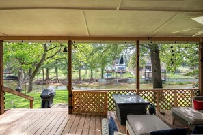 A covered outdoor deck with a view of a park, a gazebo, and a body of water. - Charming waterfront getaway with great water access. (Tool)