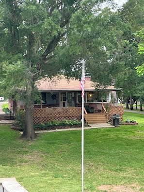 A building with a porch, surrounded by trees and a grassy area. - Charming waterfront getaway with great water access. (Tool)
