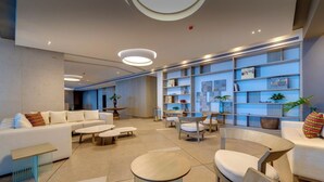 Eine moderne Lobby mit einer Couch, Sesseln, einem Couchtisch und einem Bücherregal.
