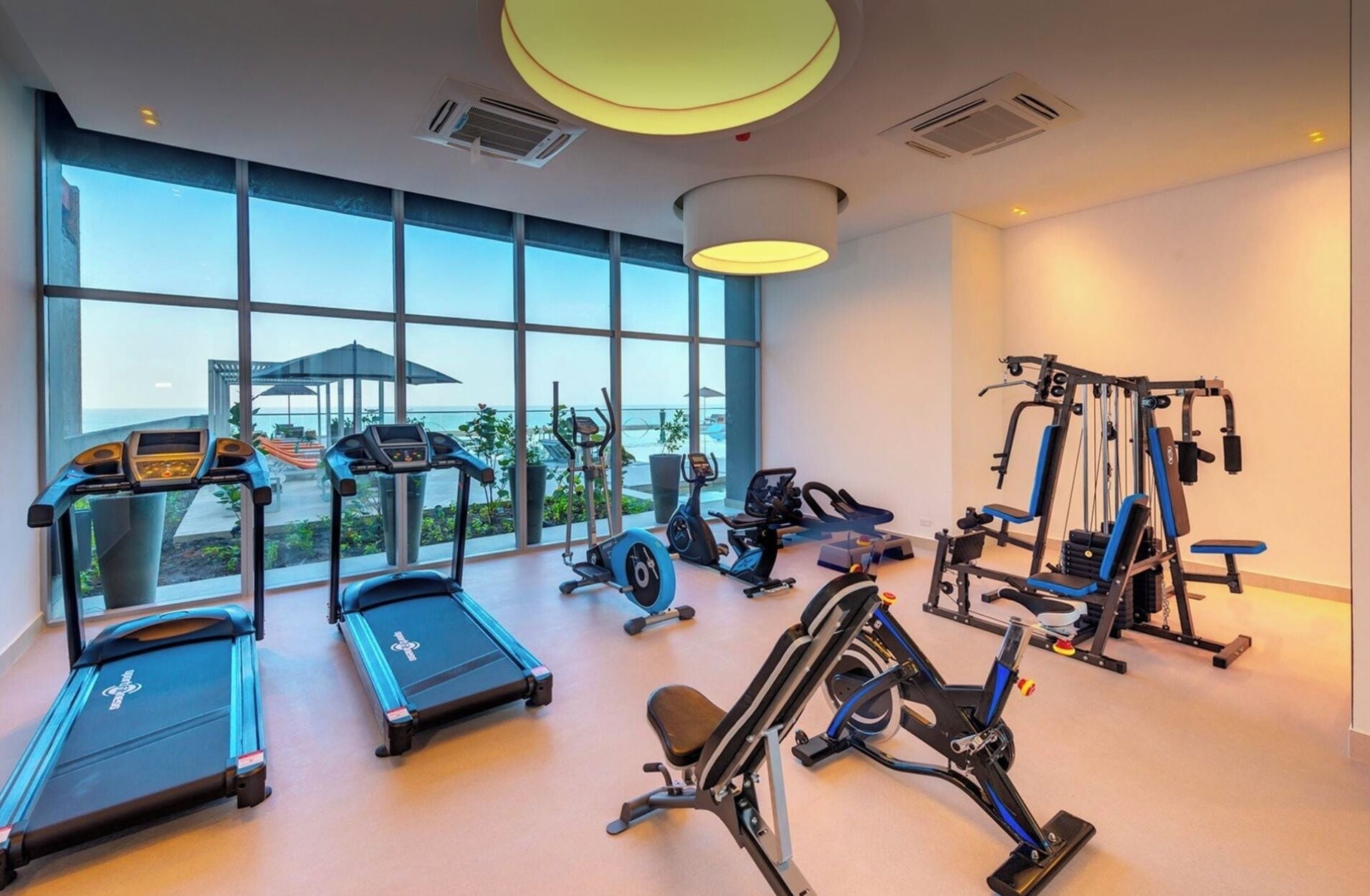 Ein Fitnessstudio mit Laufbändern, Crosstrainern und Gewichtmaschinen, großen Fenstern und Blick ins Freie.