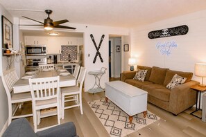 A compact living space with a dining area, kitchenette, and a seating area with a couch and ottoman. - SC 1404: Summer MTB Escape - Ride, Relax & Pool Fun (Snowshoe)