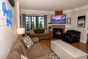 A living room with a fireplace, a flat-screen TV, and a sofa set. - SC 1404: Summer MTB Escape - Ride, Relax & Pool Fun (Snowshoe)