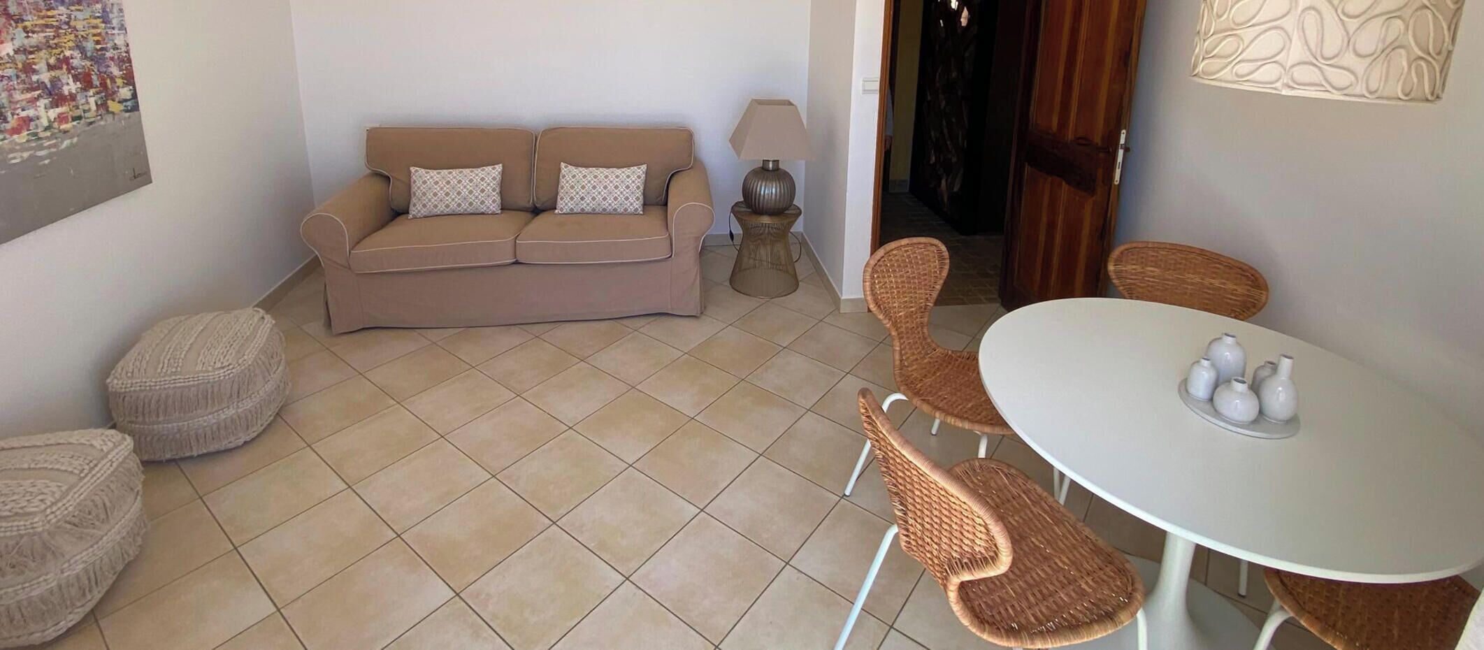 A living area with a sofa, two ottomans, a table with chairs, and a lamp.