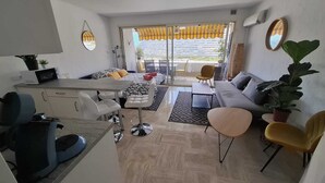 Een moderne woonkamer met een bank, salontafel en stoelen, een eethoek met een tafel en stoelen, en een glazen schuifdeur naar een buitenruimte.