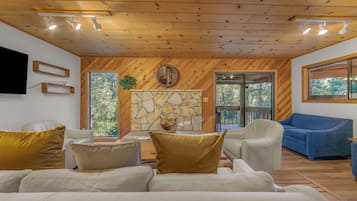 A modern living room with a stone fireplace, wooden ceiling, and large windows.