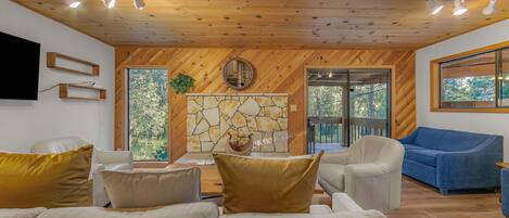 Una sala de estar moderna con chimenea de piedra, techo de madera y ventanas amplias.
