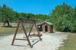 Ein hölzernes Schaukelgestell in einer Sandfläche, im Hintergrund eine kleine Holzkonstruktion.