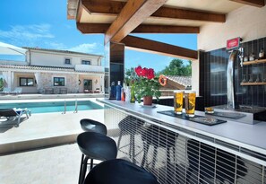 A poolside bar with a view of a pool and a building in the background. - Impressive & Spacious Villa - Private Pool, Outdoor Kitchen, Bar & Sauna - 20 mins walk to Alcudia! (Alcudia)