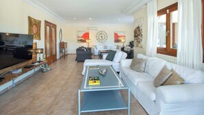 A living room with a TV, sofa, coffee table, and artwork. - Impressive & Spacious Villa - Private Pool, Outdoor Kitchen, Bar & Sauna - 20 mis walk to Alcudia! (Alcudia)