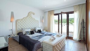 A bedroom with a large bed, a bedside table, a lamp, and a view of the outdoors. - Impressive & Spacious Villa - Private Pool, Outdoor Kitchen, Bar & Sauna - 20 mis walk to Alcudia! (Alcudia)