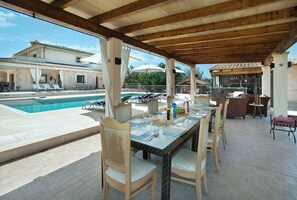 Ein Außenbereich mit Pool, Liegestühlen, einer Bar und einer überdachten Sitzgruppe.