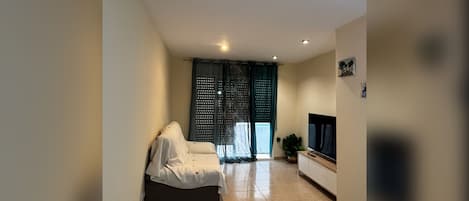 Una habitación de hotel moderna con cama, televisión, una mesita y ventana con cortinas.