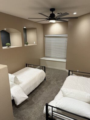 A bedroom with two single beds, a ceiling fan, a window with blinds, and a small mirror. - Peaceful Family Retreat with Hot Tub, Game Room & BBQ Near State Farm Stadium (Avondale)