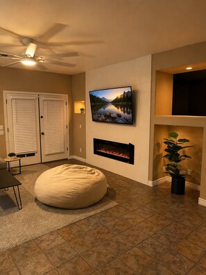 Ein Wohnzimmer mit flachbildfernseher an der Wand, Kamin, Sitzsack und Deckenventilator.
