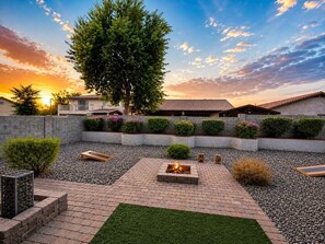 A landscaped outdoor area with a fire pit, gravel paths, and neatly trimmed bushes. - Peaceful Family Retreat with Hot Tub, Game Room & BBQ Near State Farm Stadium (Avondale)