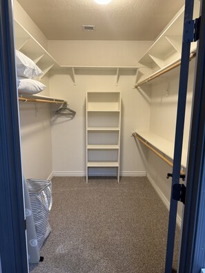 Un dressing accessible sans porte, doté d’étagères ouvertes, d’une tringle et d’un banc de rangement.