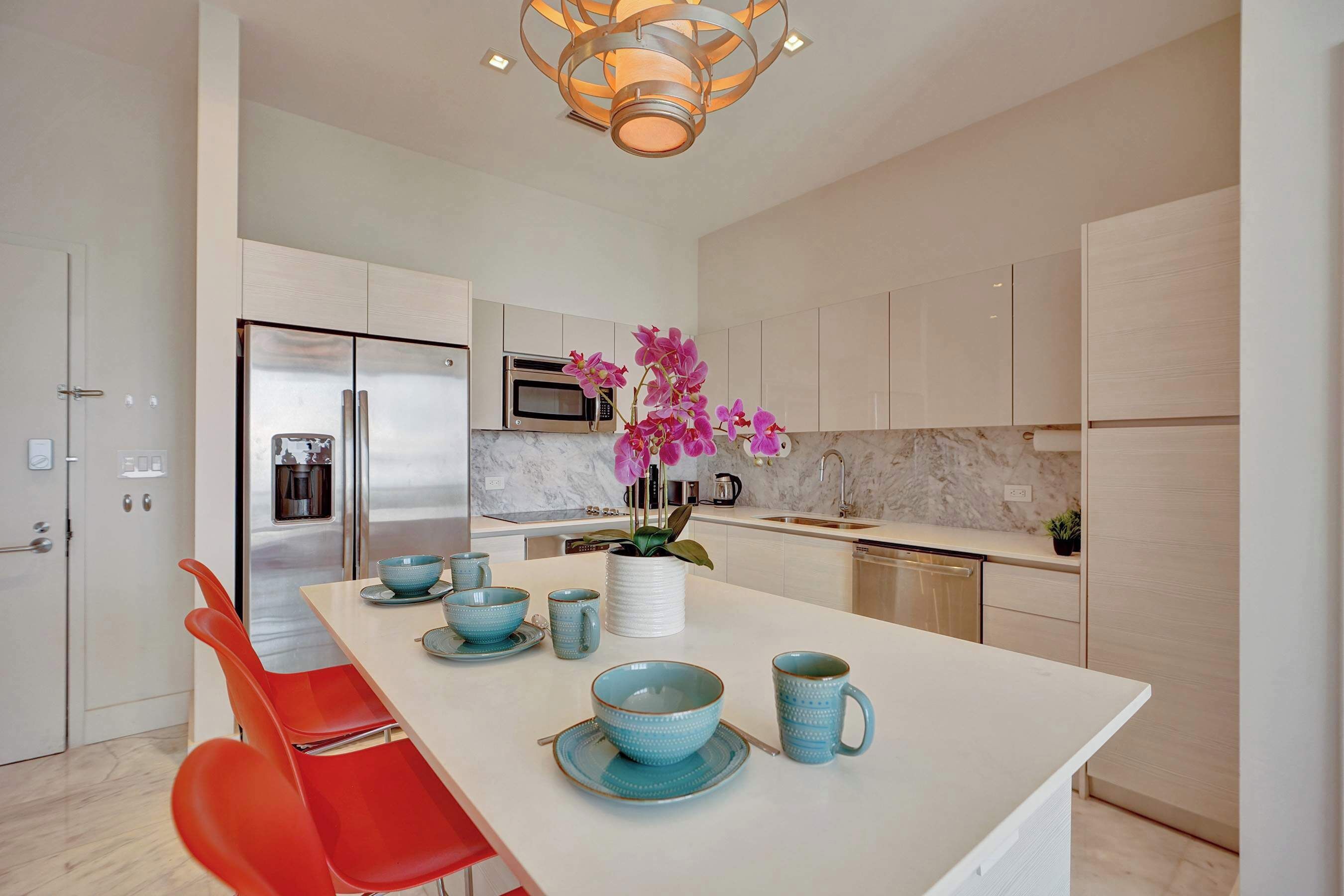 A modern kitchen with a central island, red chairs, and a vase with pink flowers.