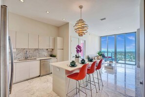 A modern kitchen with a large island, red bar stools, and a view of the city through large windows. - Luxury Penthouse | Ocean & Canal Views, Pool & Gym 3306 (Hallandale Beach)