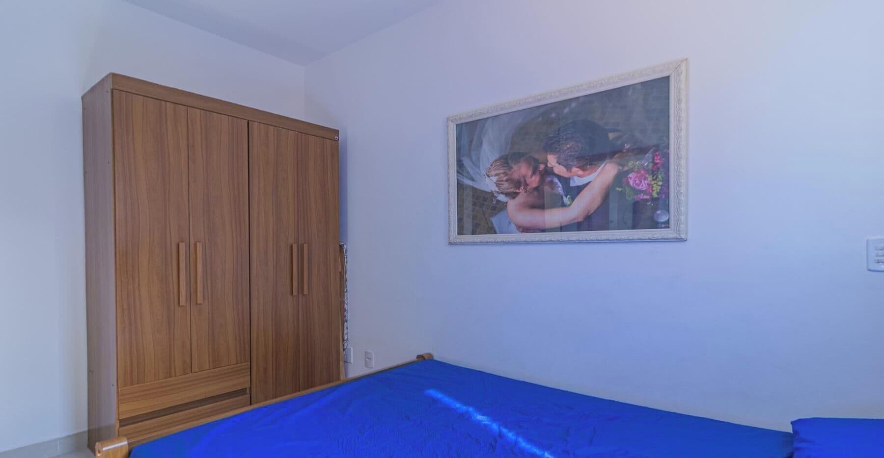 Un dormitorio con un armario de madera, una cama con cubrecama azul y un cuadro en la pared.