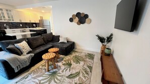 Ein modernes Wohnzimmer mit einer Couch, zwei runden Holzhockern, einem Couchtisch, einem gemusterten Teppich, einem Wandbild und einem kleinen Holznachttisch mit einer Pflanze.