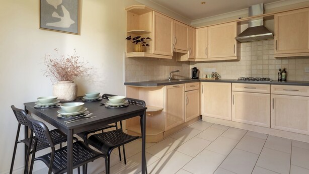 A modern kitchen with light wood cabinets, a black dining table with chairs, and a vase with dried plants on the wall. - Modern Home nr Exeter, Garden & Private Parking (Bradninch)