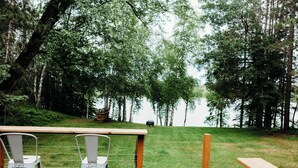 A wooden deck with metal chairs and a table, overlooking a grassy area with trees and a distant view of a body of water. - Lakefront Cabin Near Duluth (Duluth)