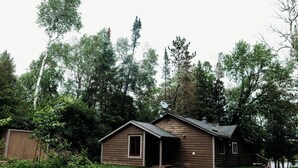A small wooden cabin with a porch, surrounded by dense trees and a grassy yard. - Lakefront Cabin Near Duluth (Duluth)