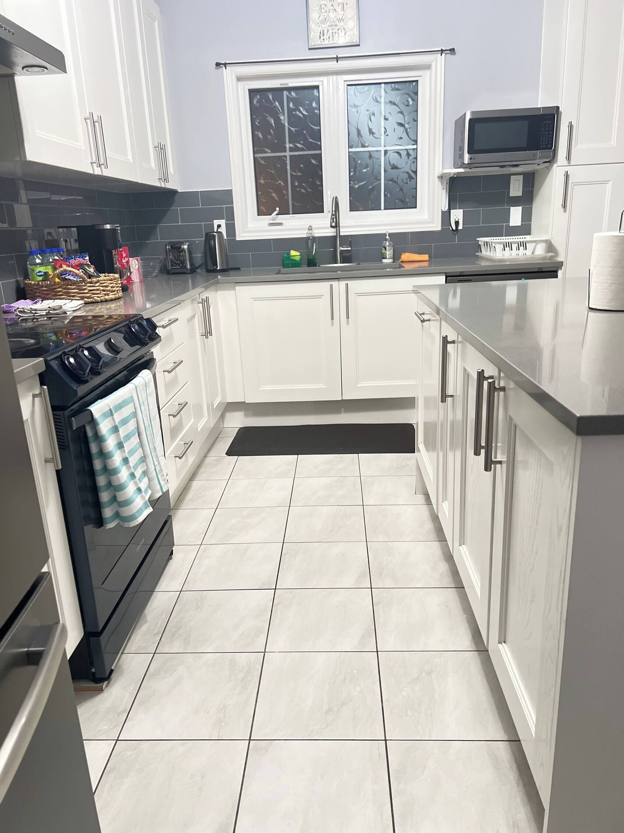 A modern kitchen with white cabinets, a black stove, a microwave, and a window above the sink.