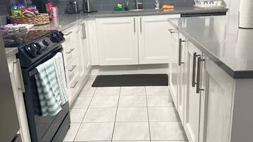 A modern kitchen with white cabinets, a black stove, a microwave, and a window above the sink.