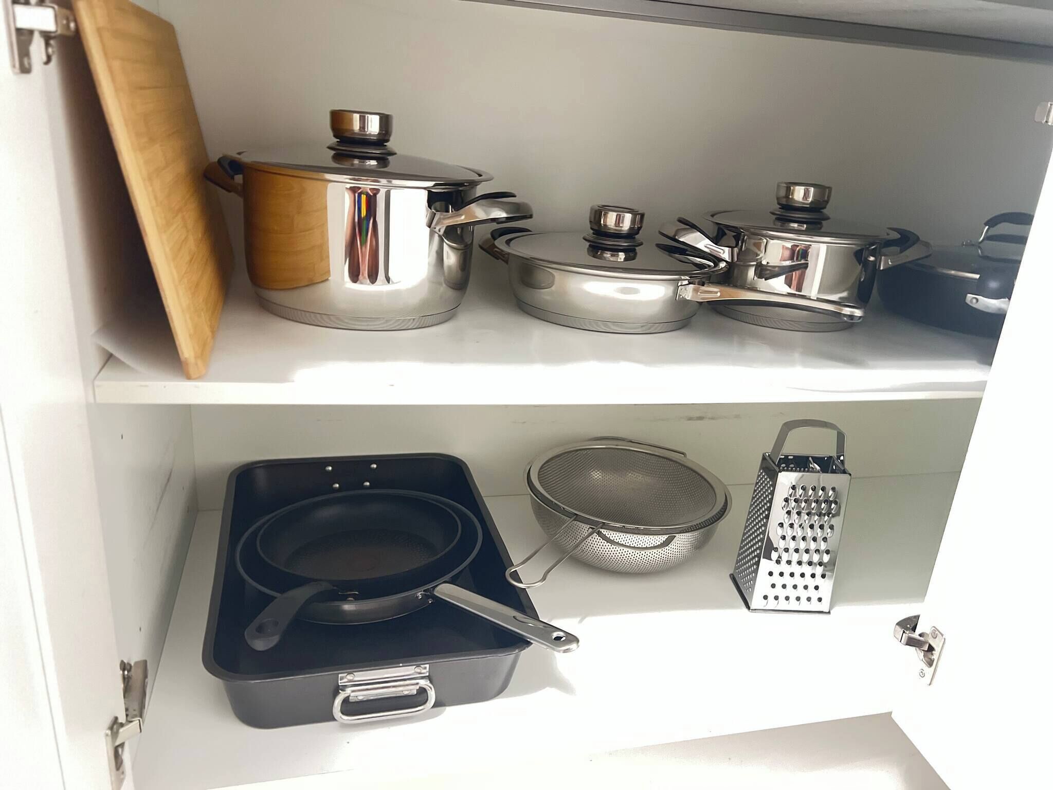 Cocina con utensilios de acero inoxidable, un rallador y un colador en estantes.