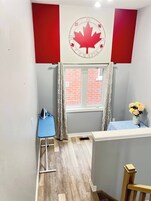 Una habitación con ventana, una mesa con un florero, un mantel azul y una decoración de hoja de arce rojo en la pared.