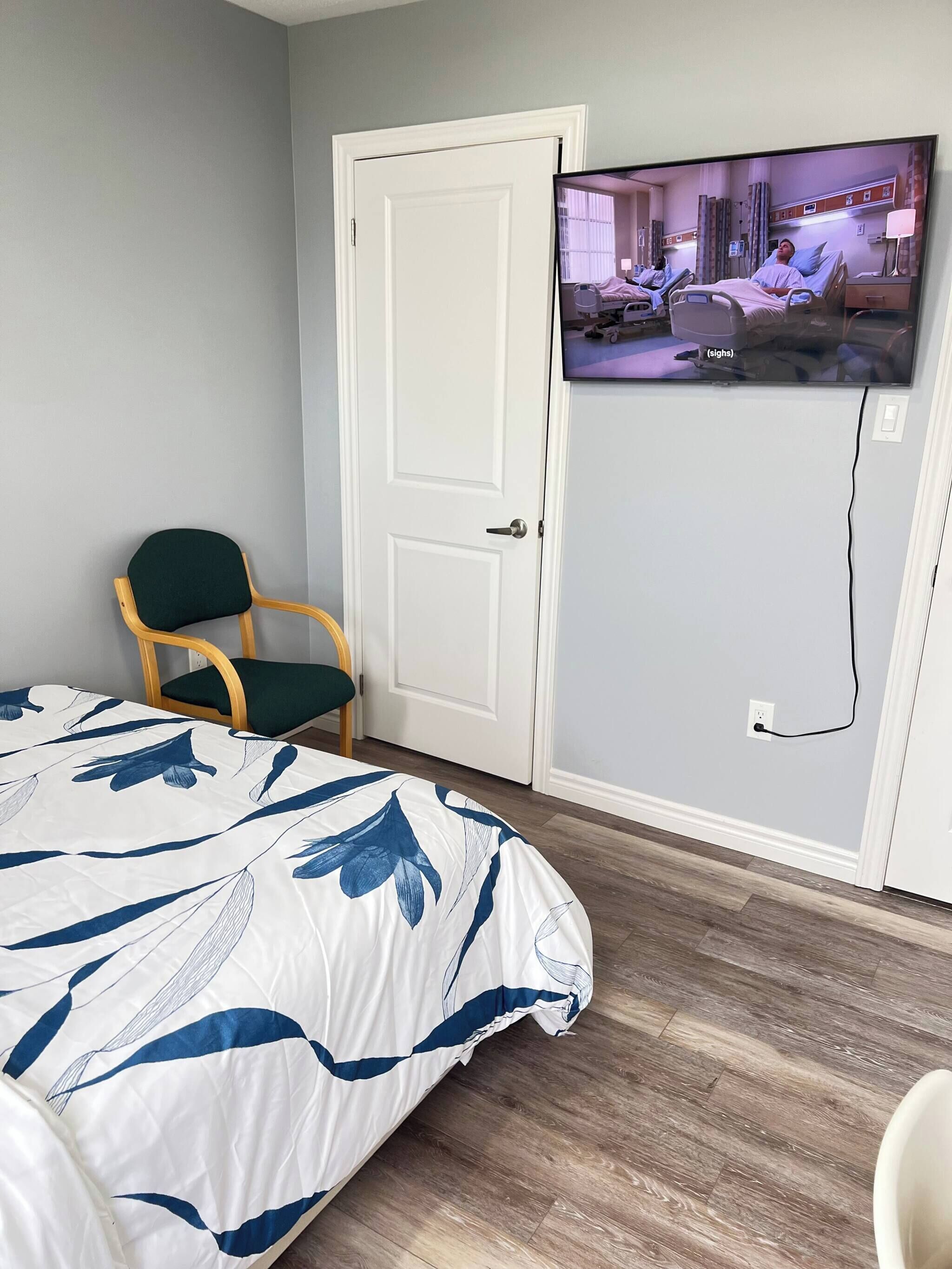 A bedroom with a bed, a television mounted on the wall, a door, and a chair.