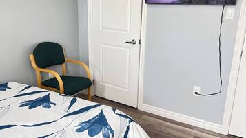 A bedroom with a bed, a television mounted on the wall, a door, and a chair.