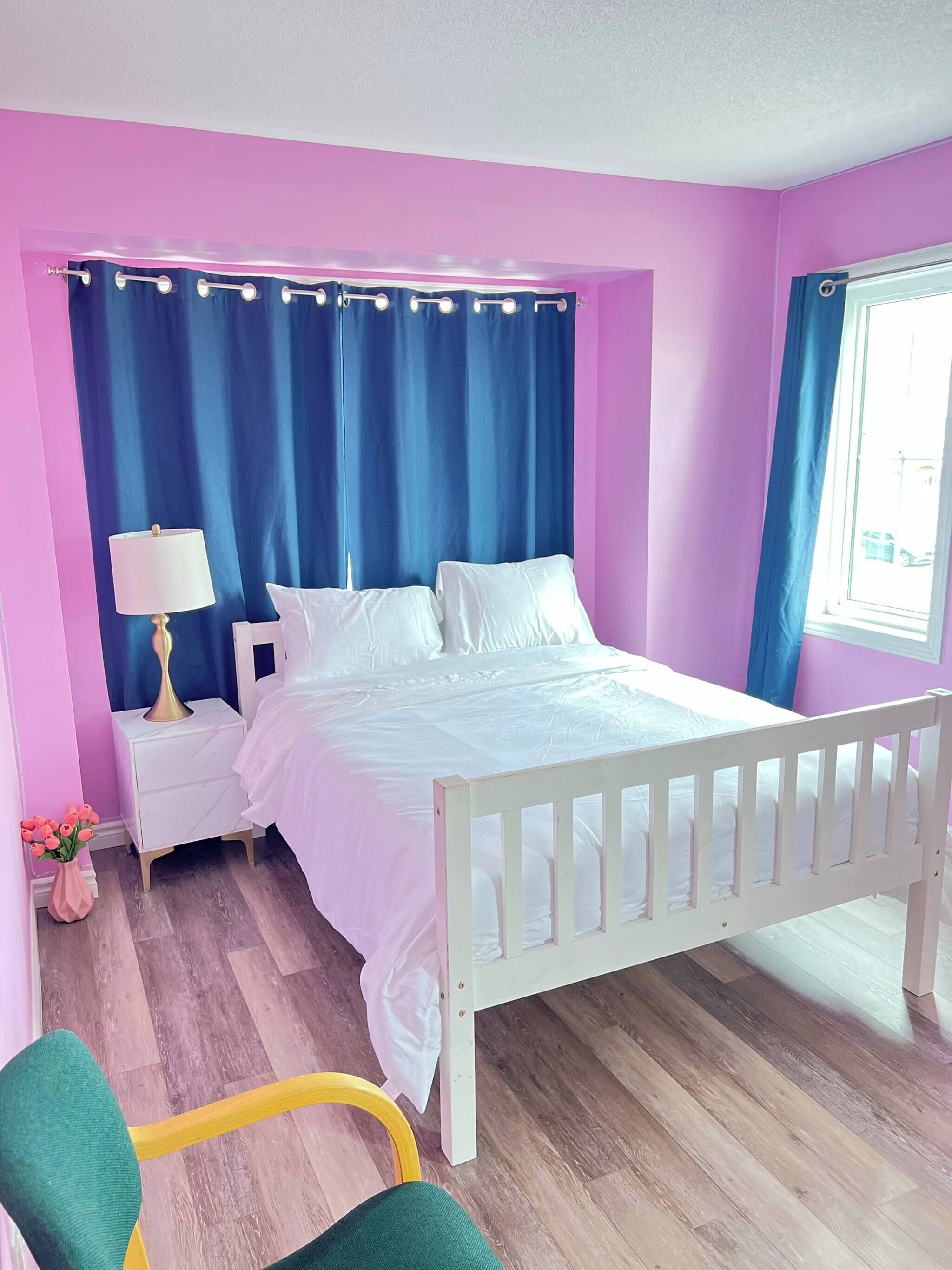 A bedroom with a bed, nightstand, lamp, chair, and a window with curtains.